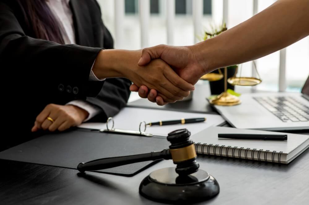 Handshake between a client and attorney in a legal office, with a gavel and legal scales on the desk, symbolizing trust and partnership in estate planning and real estate services.