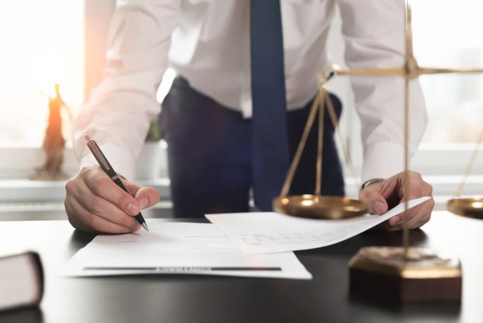 Attorney signing legal documents with scales of justice and law figurine in the background, symbolizing legal services and estate planning in Maryland.