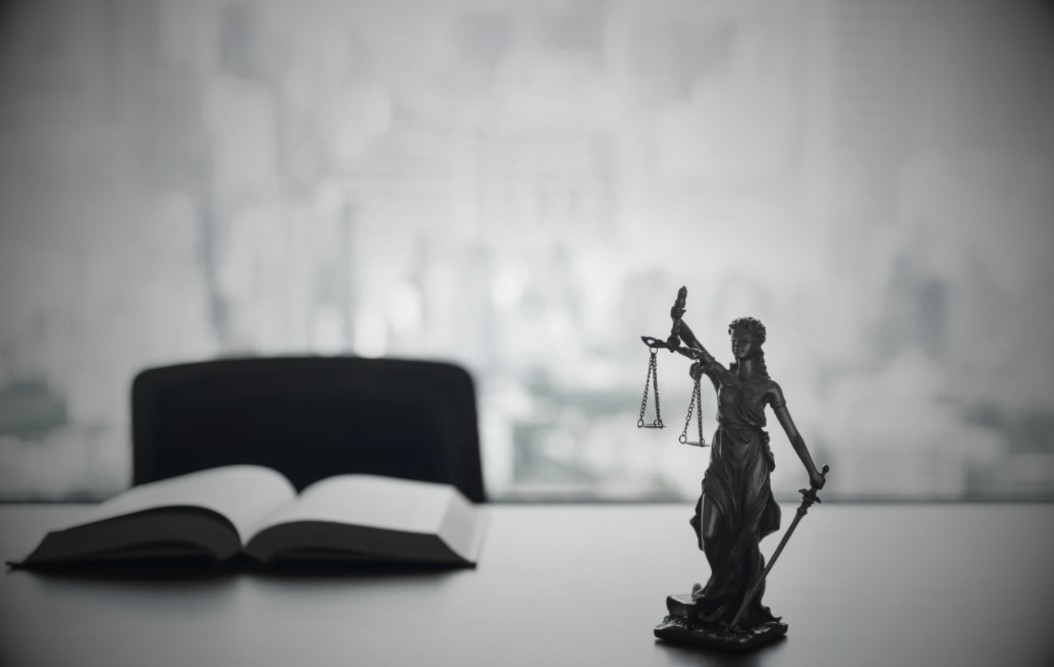 Statue of Lady Justice with scales and sword, open law book in foreground, modern office background, symbolizing legal guidance and real estate law services by Peter S. Buas.