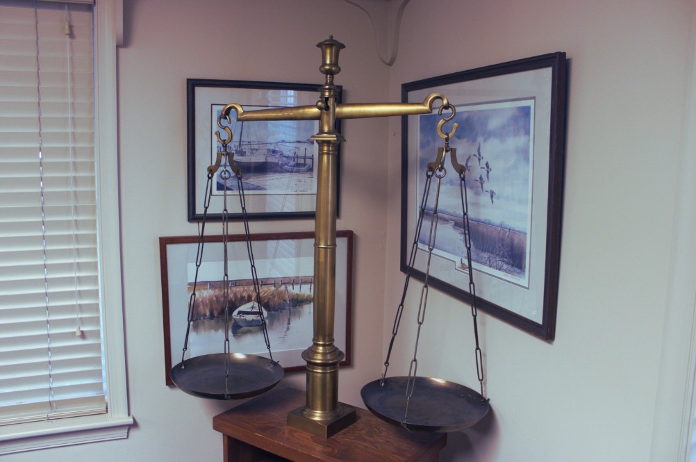 Brass balance scale symbolizing justice in a legal office, surrounded by framed maritime artwork, reflecting Peter S. Buas's expertise in tax sale foreclosures.