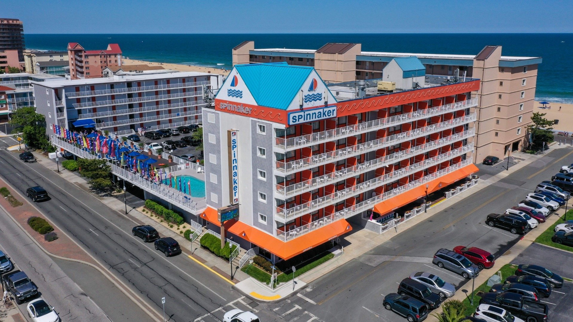 Hotel Spinnaker building with orange accents and balconies, pool area with colorful flags, adjacent to beach and ocean, showcasing real estate settlement services context.